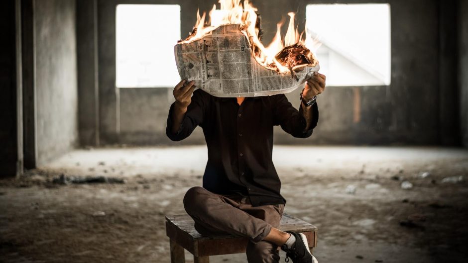 An individual gripping a newspaper that's on fire, flames flickering from the paper.